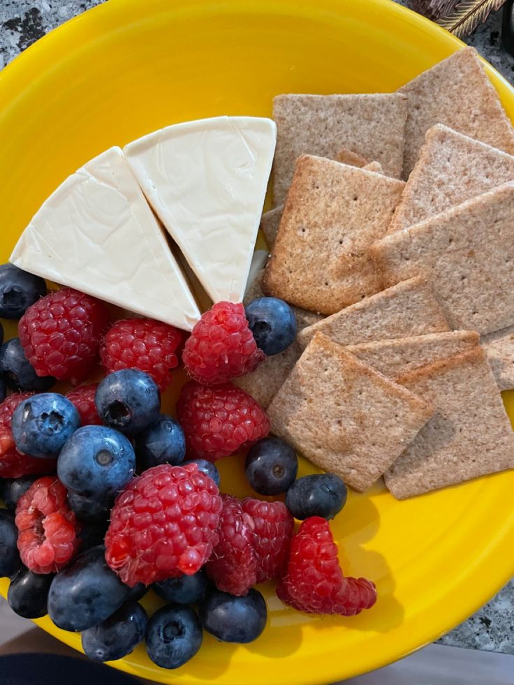 a yellow plate topped with crackers, berries and cheese