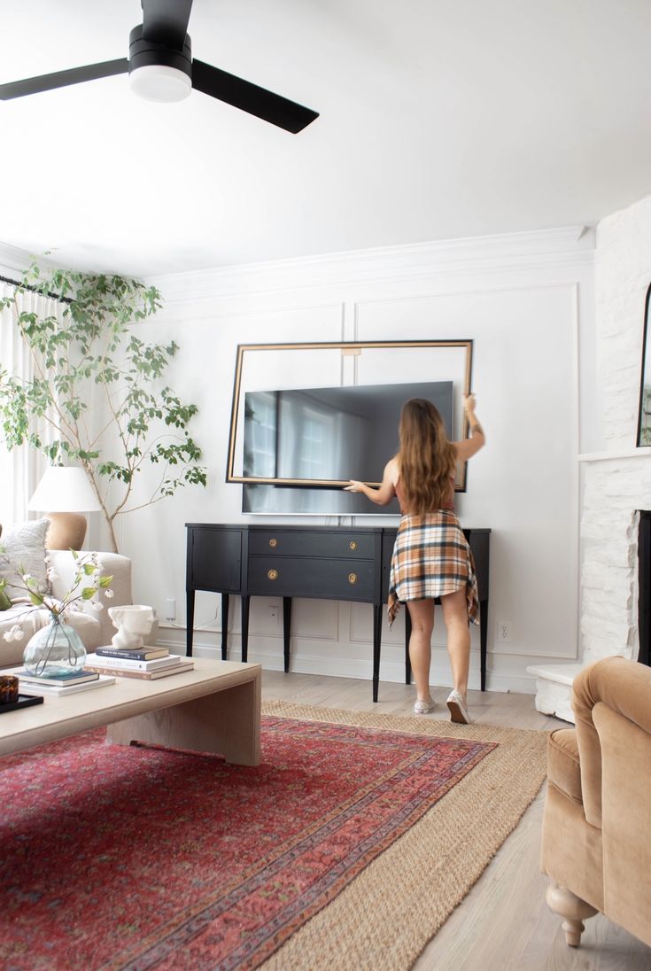 a woman is standing in front of a tv and looking into the living room with her back to the camera