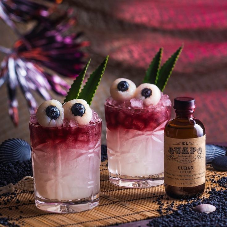 two glasses filled with liquid and eyeballs sitting on top of a bamboo mat next to a bottle