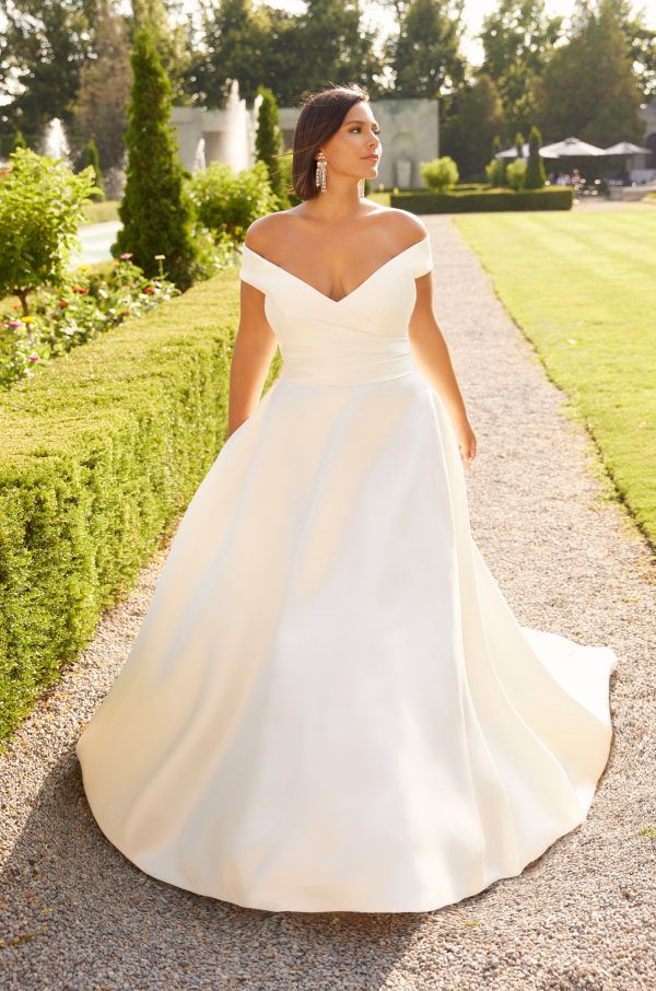 a woman in a white wedding dress is walking down the path with her hand on her hip