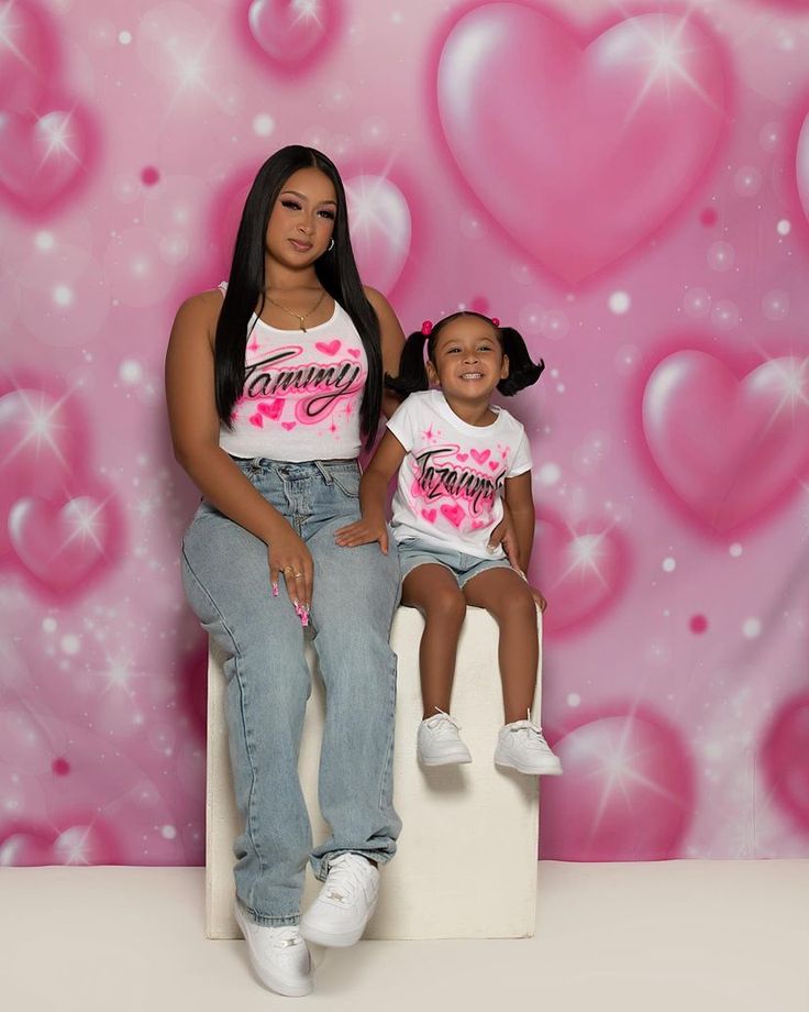 a mother and daughter posing for a photo in front of a pink background with hearts