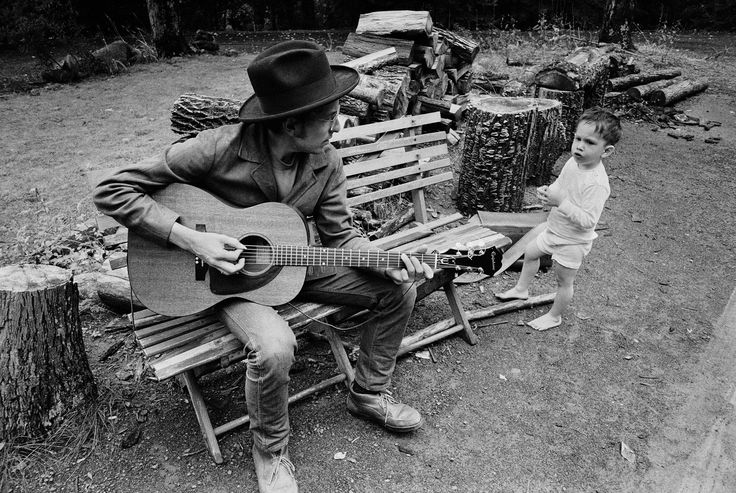 a man sitting on top of a wooden bench next to a little boy holding a guitar