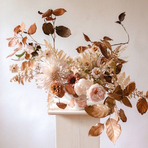 a vase filled with lots of flowers sitting on top of a white table next to a wall