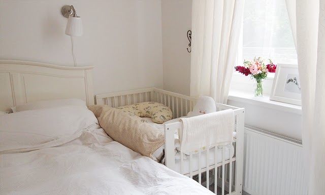 a white crib next to a window in a room with flowers on the windowsill