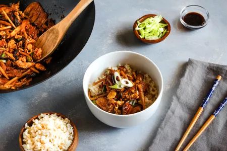 two bowls filled with food next to rice and chopsticks on a table top