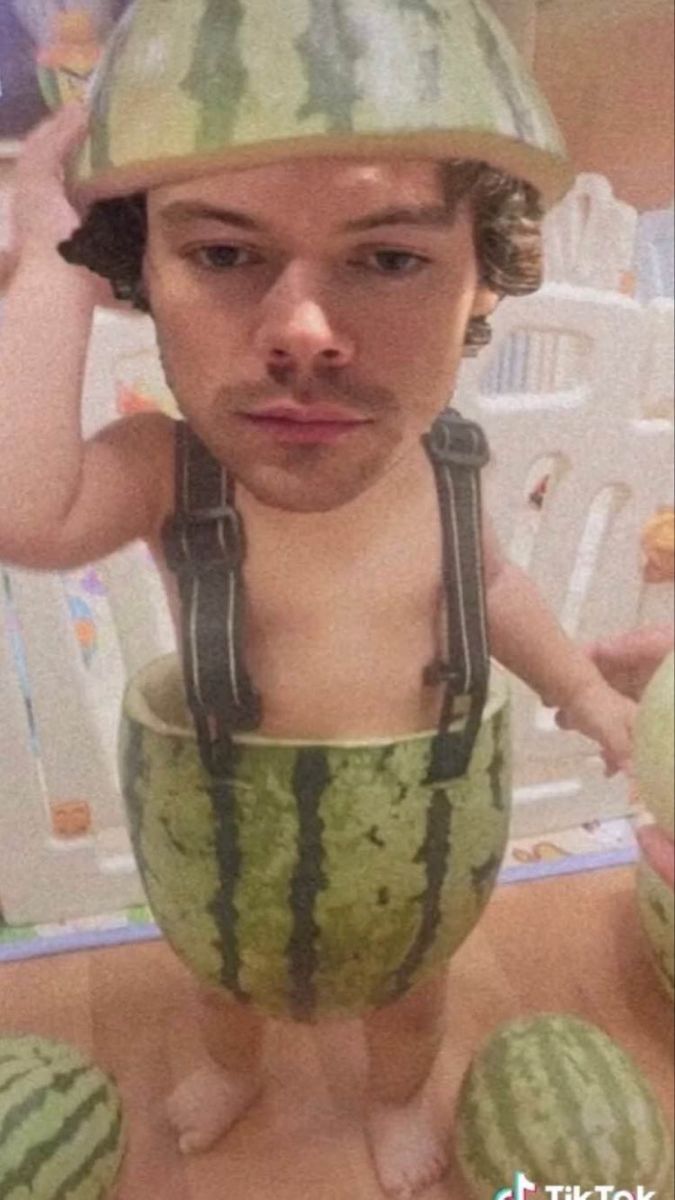 a young boy wearing a watermelon helmet on his head and holding two melons in front of him