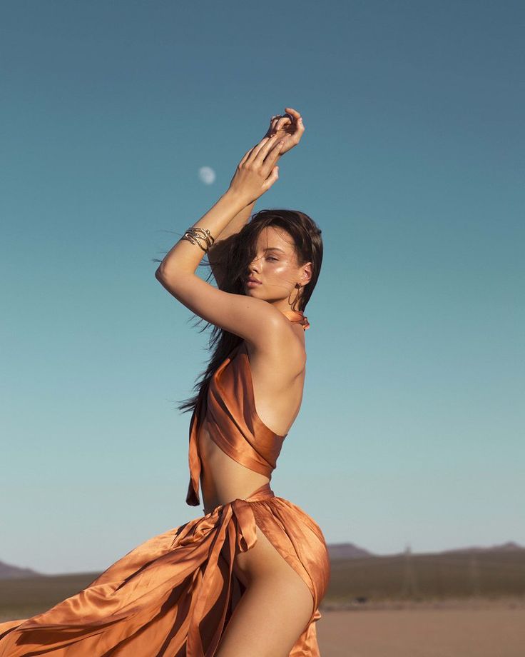 a woman in an orange dress is posing on the beach with her legs spread out