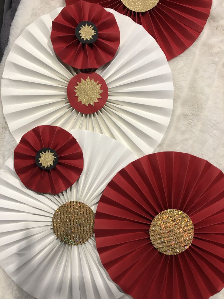 three red and white paper fans with gold glitters on them, sitting on a furnishing