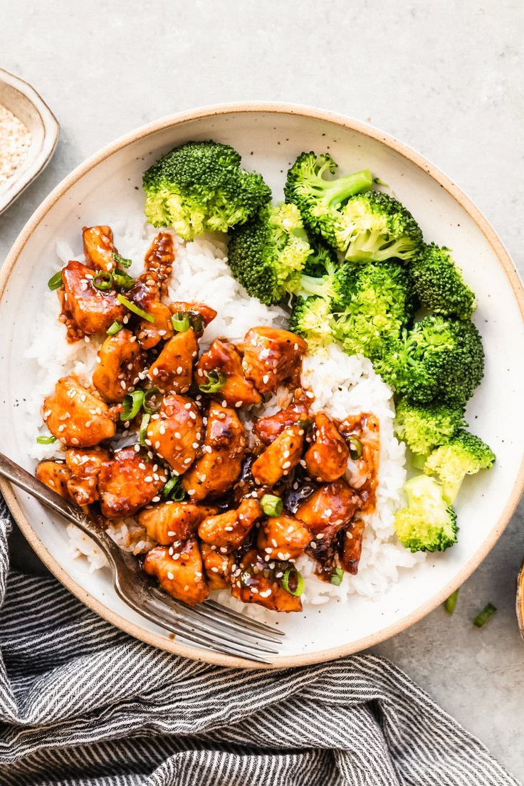 a white plate topped with chicken and broccoli covered in sesame seeds on top of rice