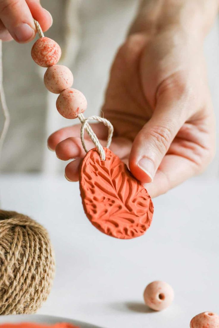 a person is holding a small red leaf charm in front of some string and beads