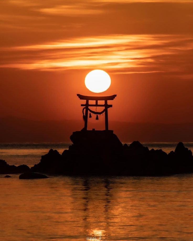 the sun is setting behind a statue in the water