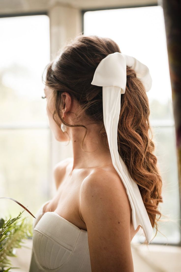 a woman wearing a white dress with a bow in her hair looking out the window