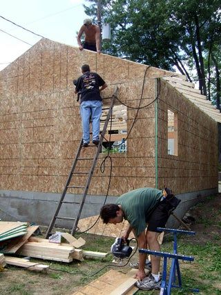 two men are working on the roof of a house that is being built with straw