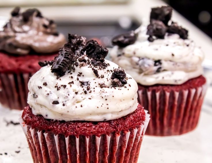 three red velvet cupcakes with white frosting and oreo cookies on top