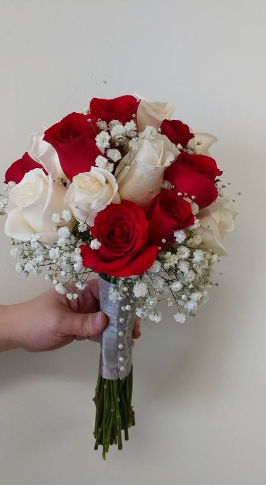 a person holding a bouquet of red and white roses in their left hand with baby's breath