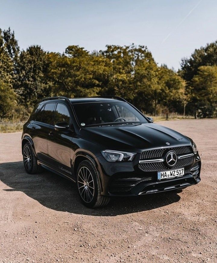 a black mercedes gle is parked in the middle of a dirt lot with trees behind it