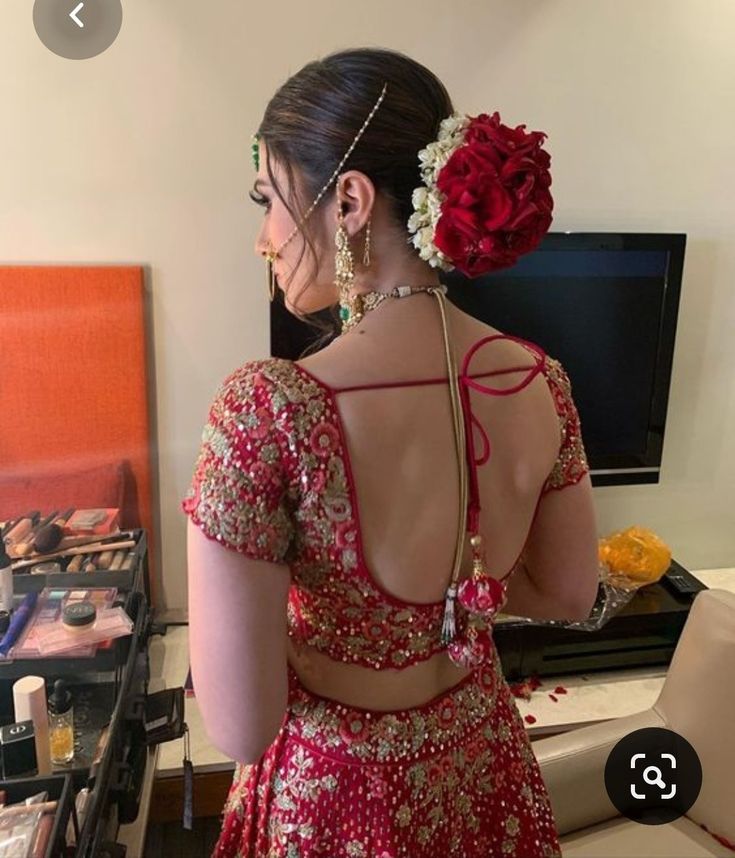 a woman in a red and gold lehenga with flowers on her head looking into the mirror