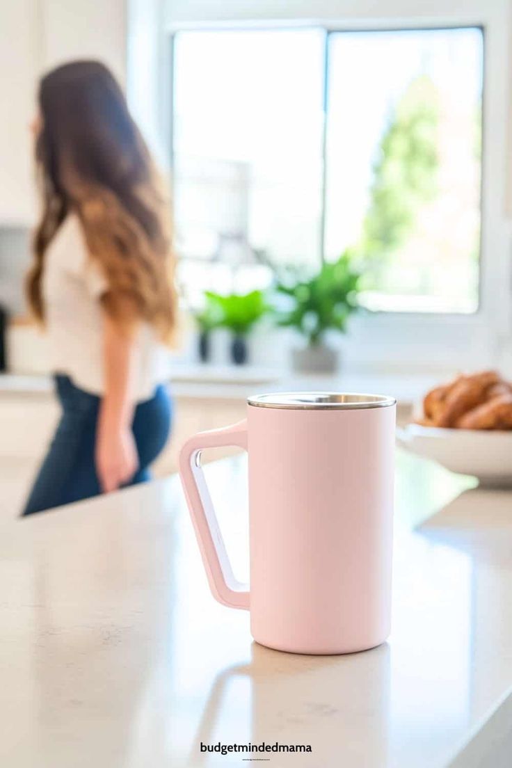 a woman sitting on the kitchen counter next to a pink coffee mug with her back turned