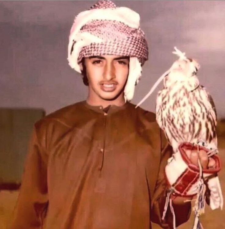 a man holding an owl on his arm in front of the camera and wearing a hat