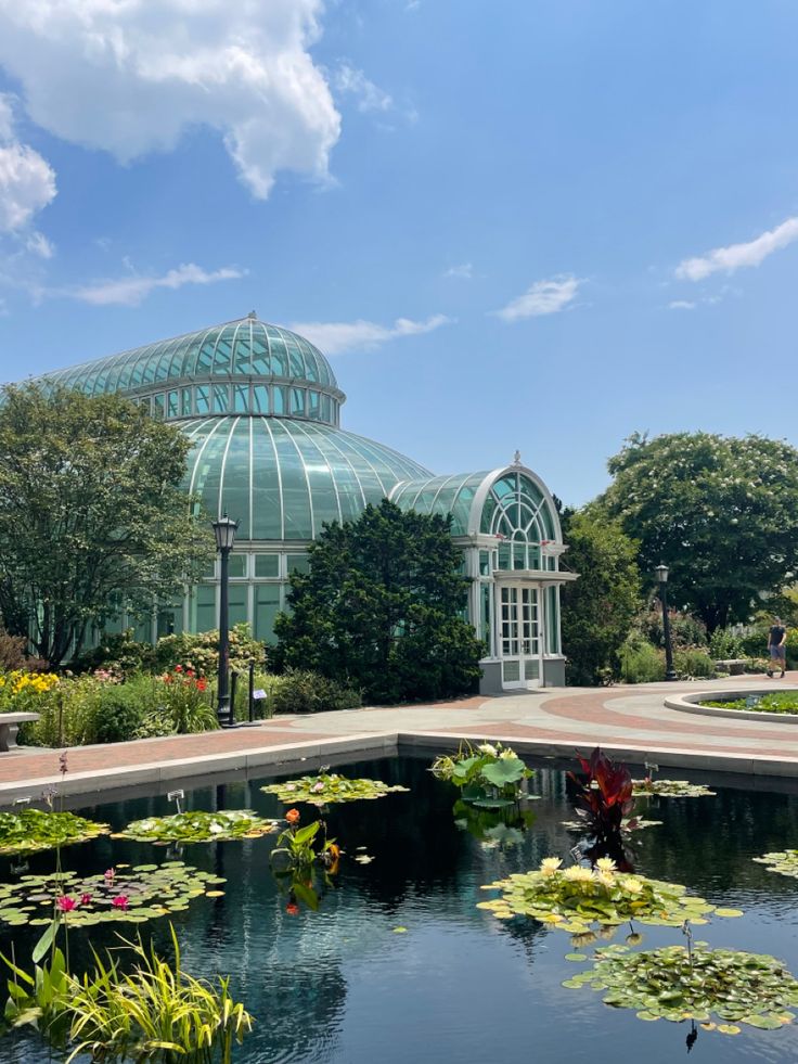 a pond in front of a glass house with water lilies and lily pads on the ground