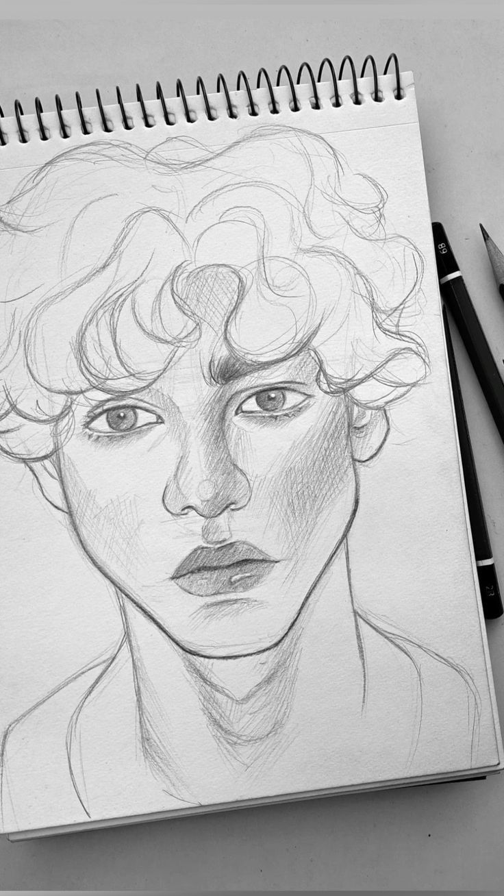 a pencil drawing of a man's face with curly hair and blue eyes on a notepad