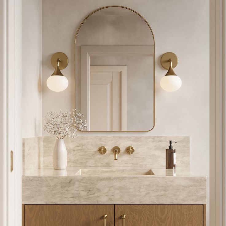 a bathroom vanity with marble counter top and gold faucet, mirror above it