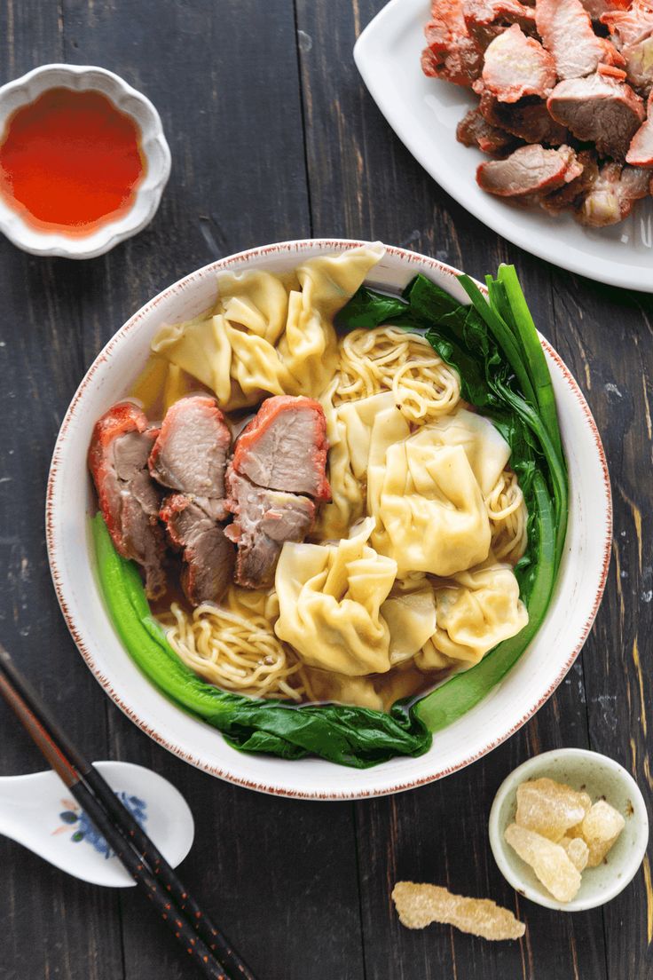 a bowl filled with meat and noodles next to chopsticks on a wooden table