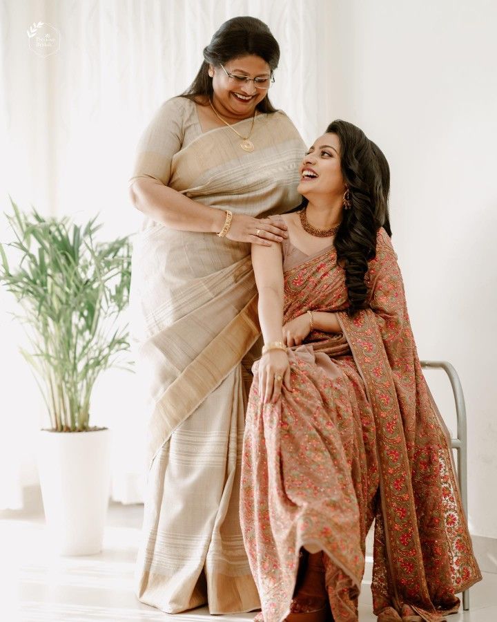 two women sitting next to each other in front of a potted plant and smiling