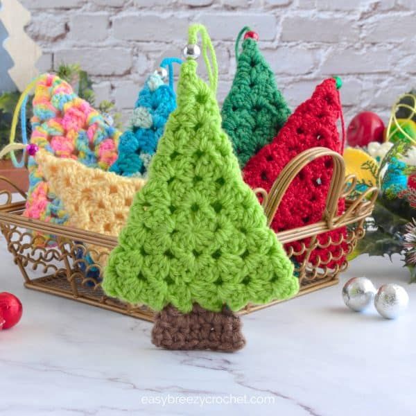 crocheted christmas tree ornaments in a basket on a table next to other holiday decorations