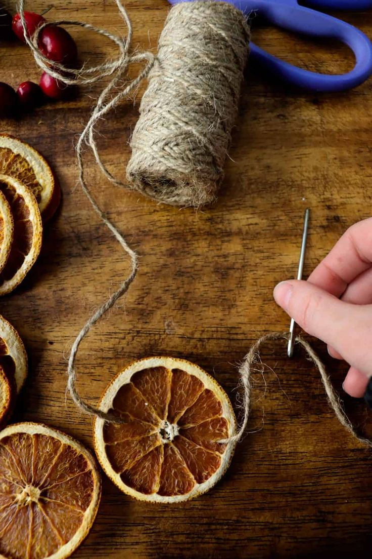 someone stringing orange slices with twine on a wooden table next to some scissors