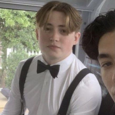 two young men wearing suspenders and bow ties sitting in a car looking at the camera