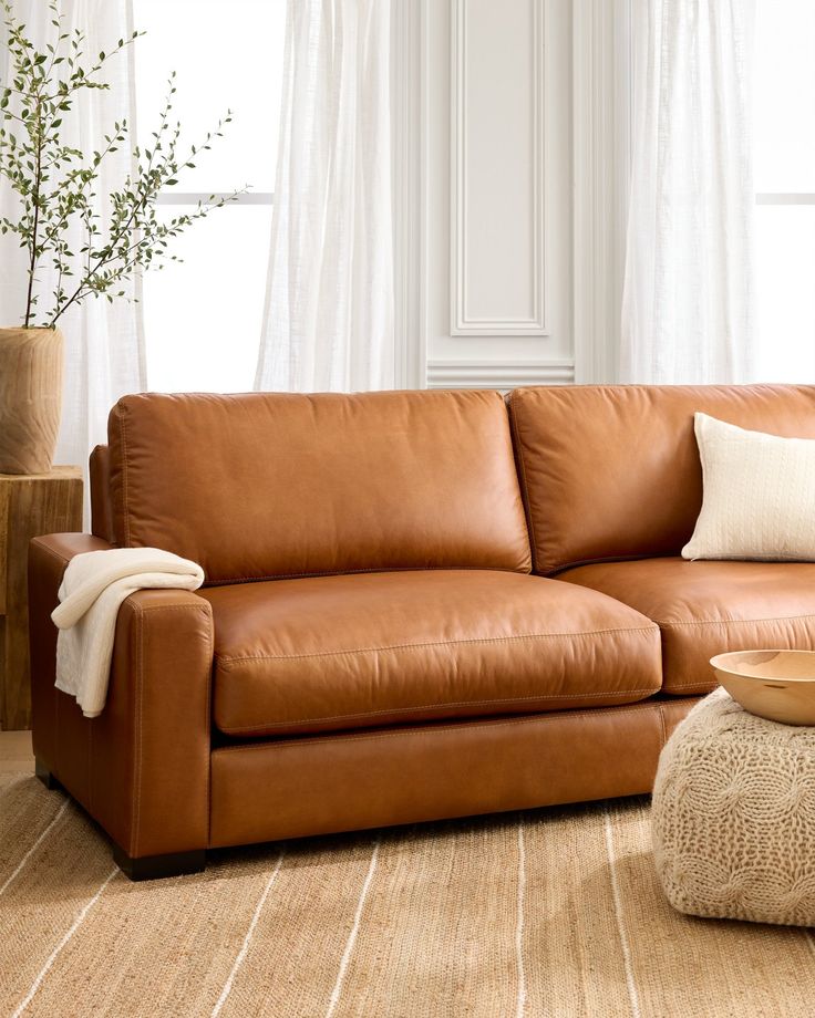 a brown leather couch sitting in front of a white window next to a coffee table