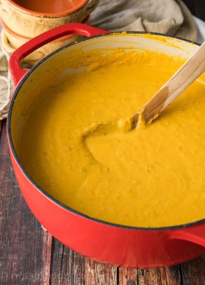 a red pot filled with yellow soup and a wooden spoon