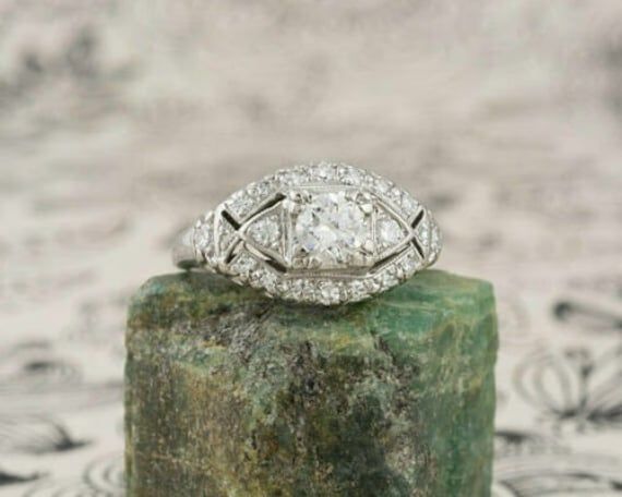 an antique style diamond ring sitting on top of a mossy green stone block,