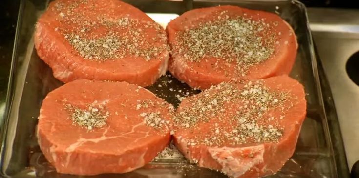 four pieces of raw meat sitting on top of a metal pan covered in seasoning