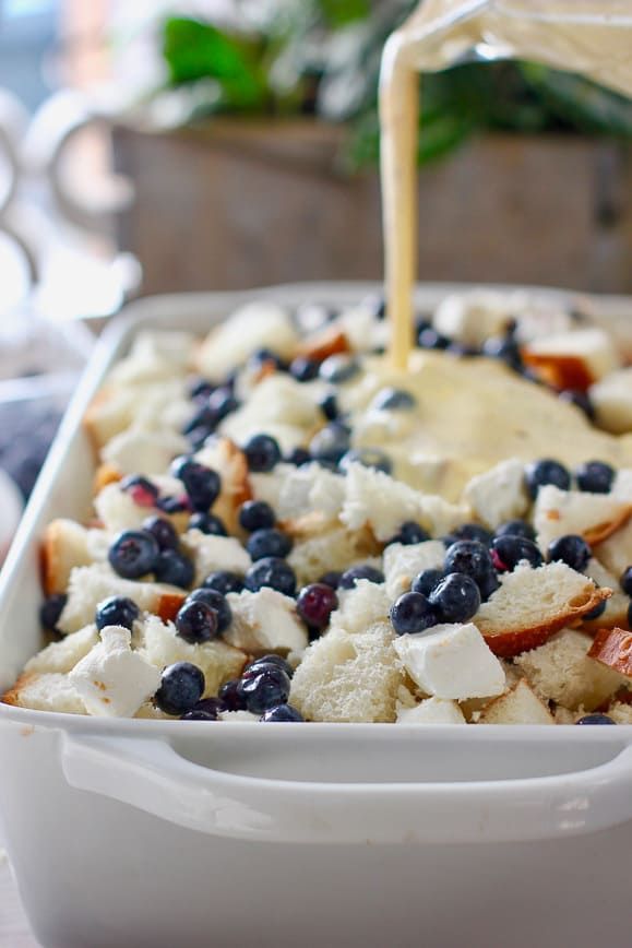 blueberries and cheese are being drizzled over bread in a casserole dish