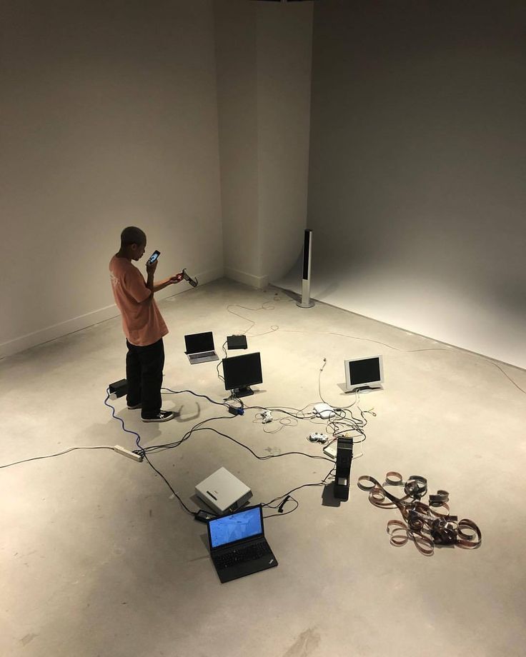 a man standing in an empty room with several laptops connected to wires and cords