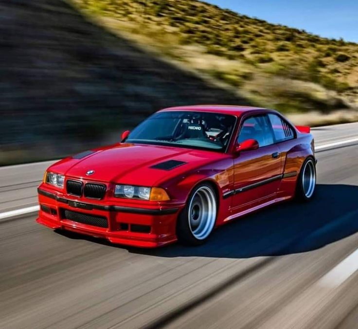 a red car driving down the road with mountains in the background