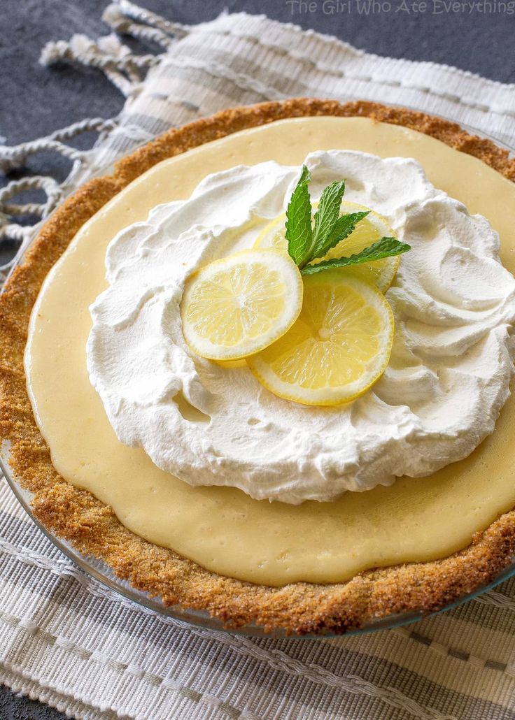 a pie with lemons and whipped cream on top is sitting on a tablecloth