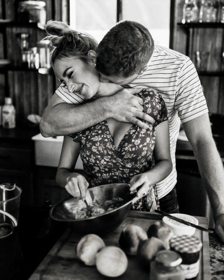 a man hugging a woman in the kitchen while she is mixing something into a bowl