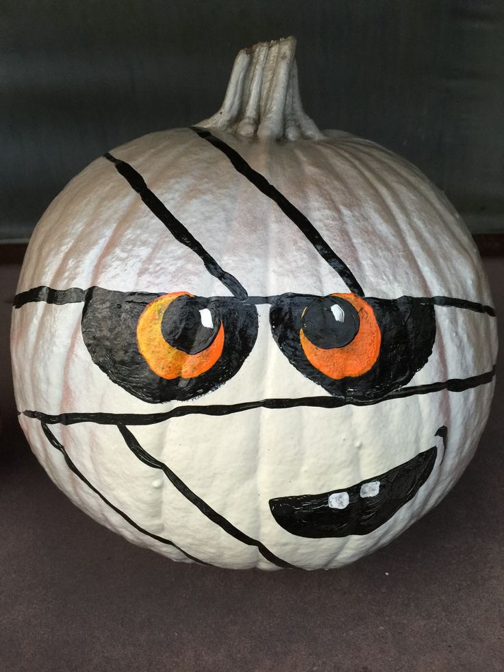 a white pumpkin with orange eyes and black lines painted on it's face is sitting on the floor