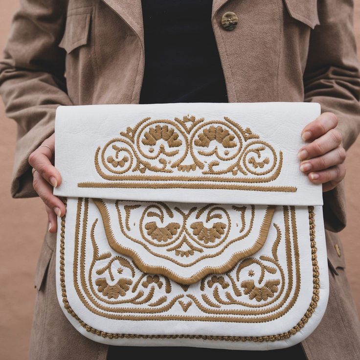 In Morocco, hand embroidery serves as a thread connecting generations, with mothers teaching daughters the craft. Embroidered designs can be found on various items in the souks—from handkerchiefs to poufs and bags—and the designs differ from city to city. This satchel, the perfect size for books, has proven itself a versatile companion for any adventure. 10" tall, 11" wide Detachable shoulder strap Embroidered leather Traditional White Travel Bag, Embroidered Cream Clutch Bag, Traditional White Shoulder Bag For Travel, White Rectangular Bag With Machine Embroidery, White Rectangular Bags With Machine Embroidery, Artisan Embroidered Pouch Bag, Traditional Handmade Cream Bags, Embroidered Cream Shoulder Bag As Gift, Traditional White Embroidered Shoulder Bag