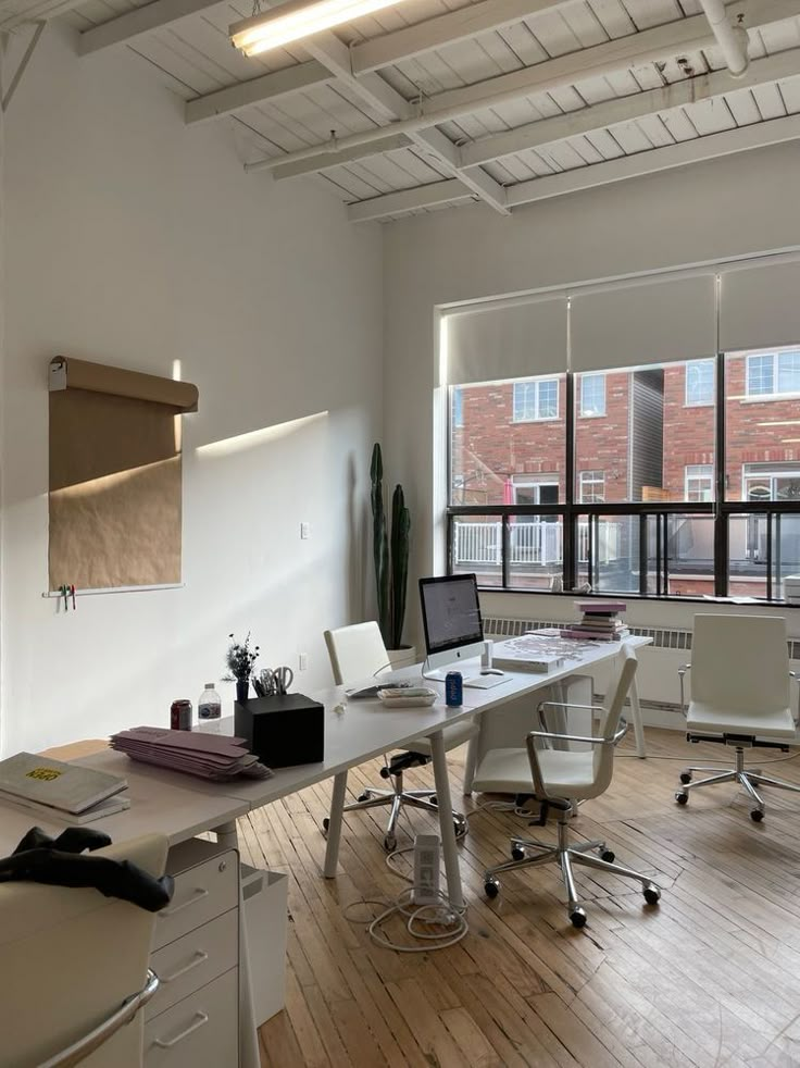 an office with white desks and chairs in front of large windows