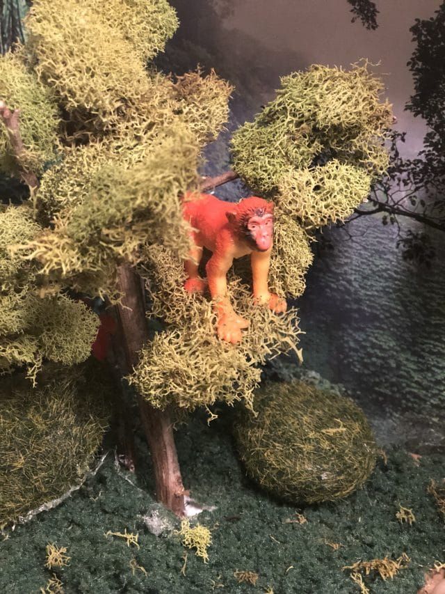 a toy monkey sitting on top of a moss covered tree