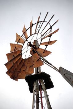 an old rusty windmill sitting on top of a wooden pole in front of a cloudy sky