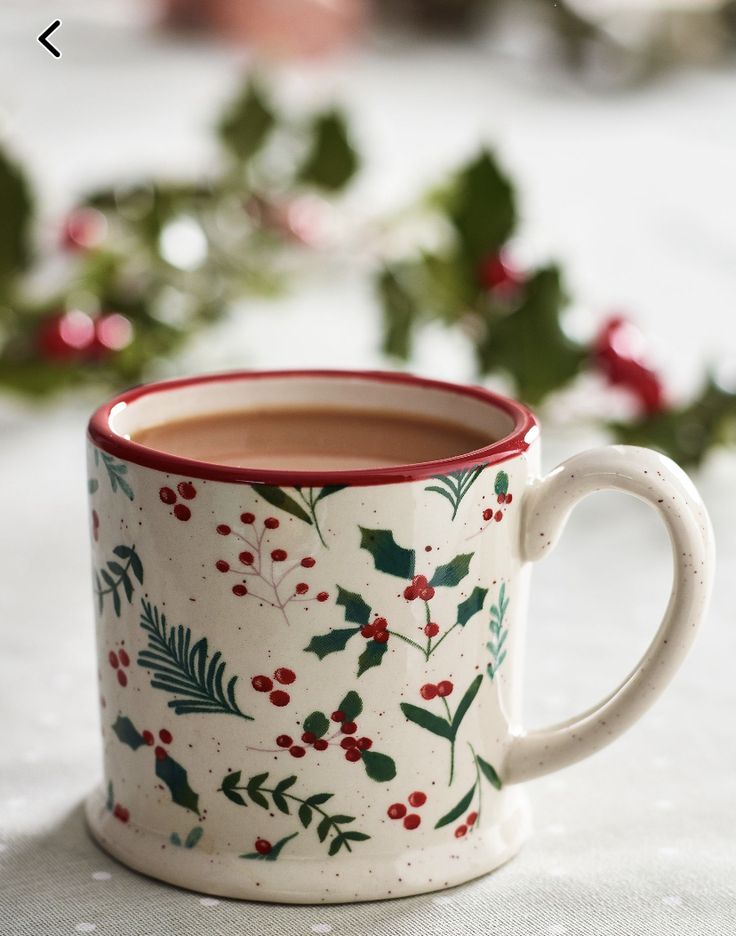 a cup of hot chocolate sits on a table with holly and red berries around it