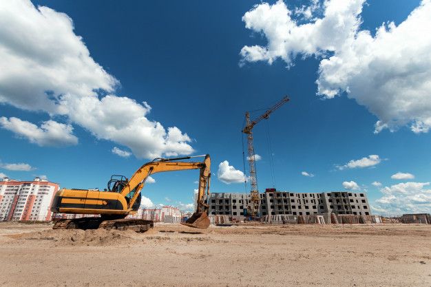 a large yellow construction vehicle sitting in the middle of a dirt field next to tall buildings