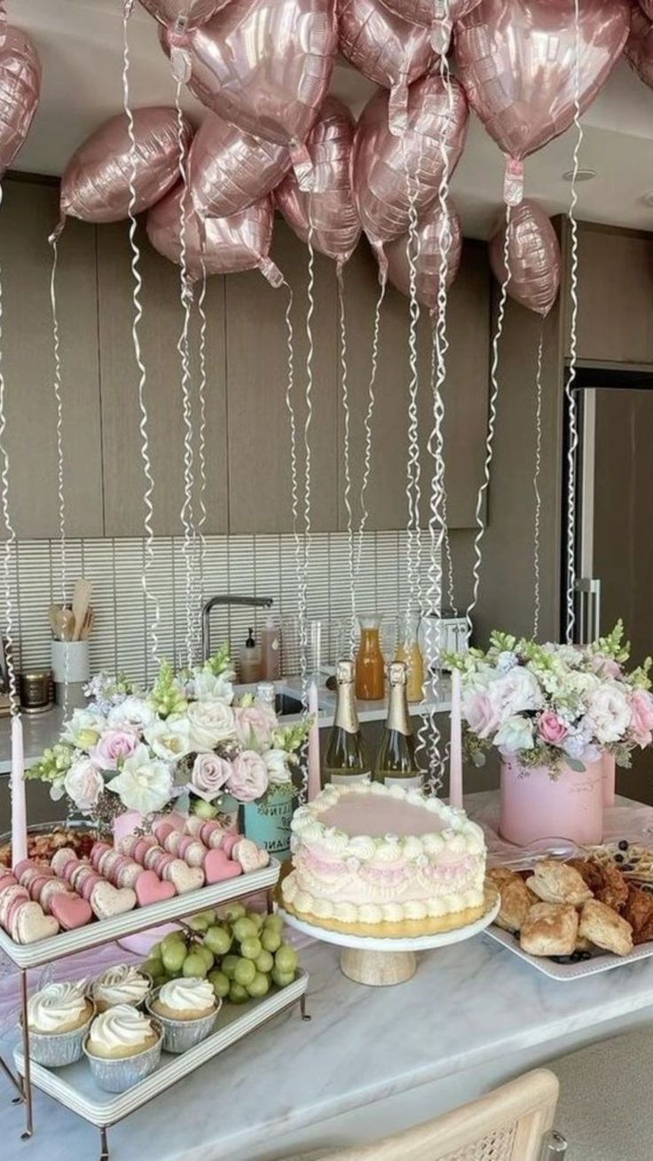 a table topped with lots of desserts and balloons hanging from the ceiling above it