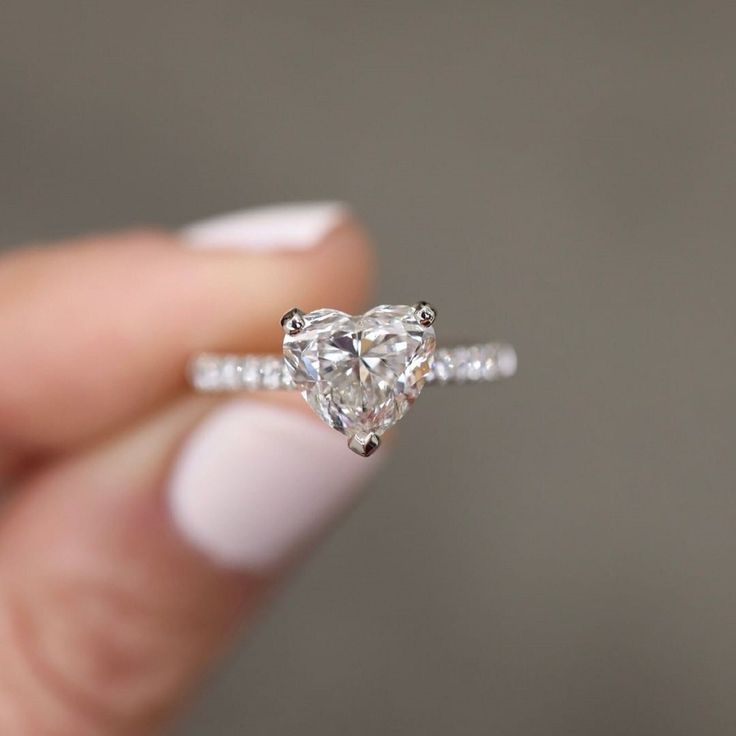 a woman's hand holding an engagement ring with a heart shaped diamond on it