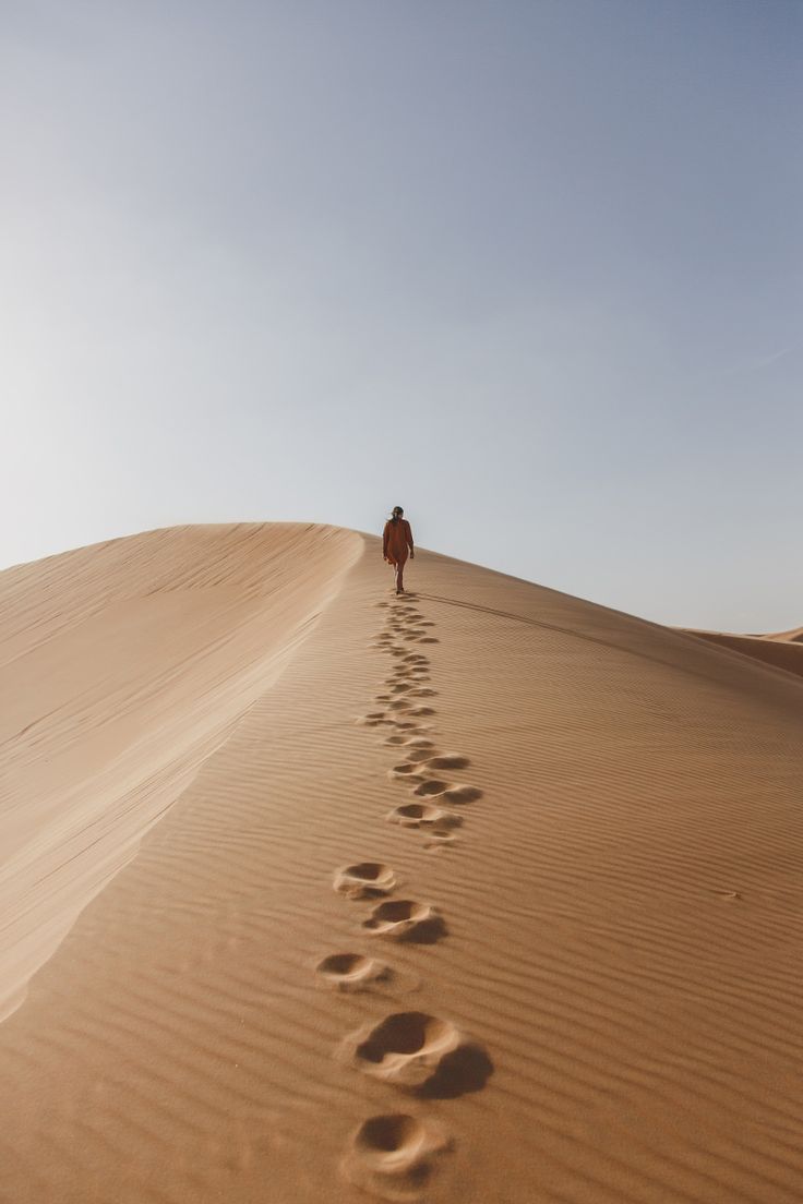 a person walking down a sandy hill with footprints in the sand